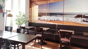 A modern dining area with a large window overlooking the beach, wooden flooring, and dark-toned furniture. - H33 hôtel (Nice)