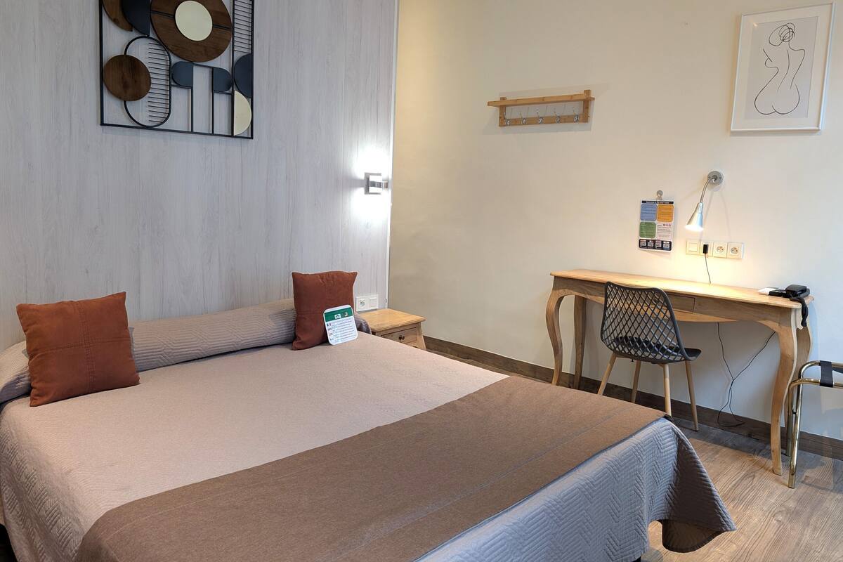 A hotel room with a bed, a desk, a chair, a lamp, and a wall art piece.
