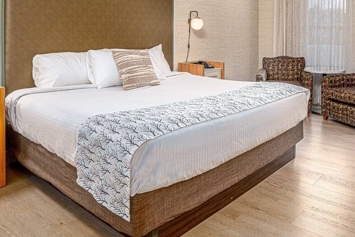 A hotel room with a large bed, a bedside table with a lamp, a chair, and a small table.