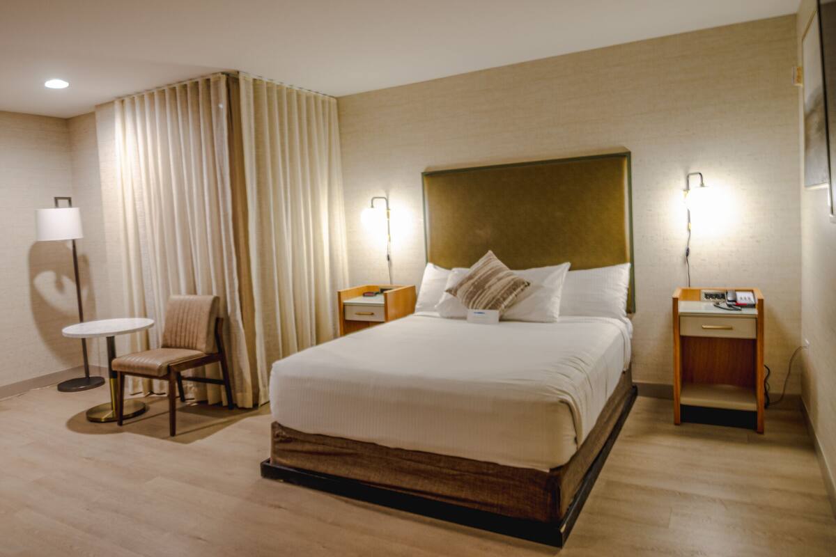 A hotel room with a large bed, two bedside tables, a chair, a lamp, and a curtain.