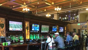 Zona de bar con varias pantallas mostrando eventos deportivos, taburetes y una mesa con salsas y aderezos.