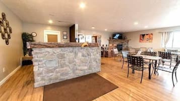 A living room with a stone accent wall, wooden flooring, a dining area with chairs and a table, and a fireplace.