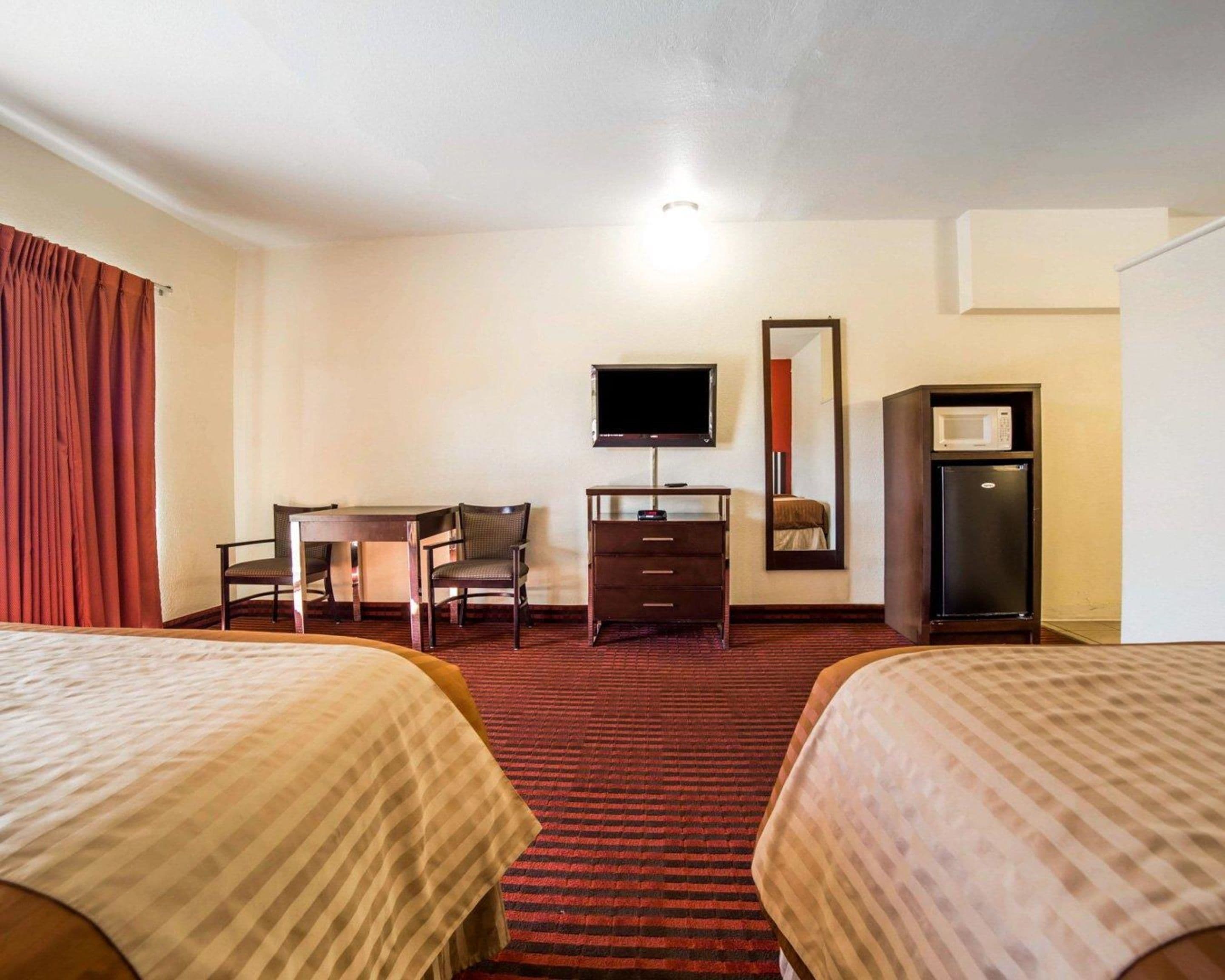 Une chambre d’hôtel avec deux lits, un bureau, une chaise, une télévision, une commode et un four à micro-ondes.