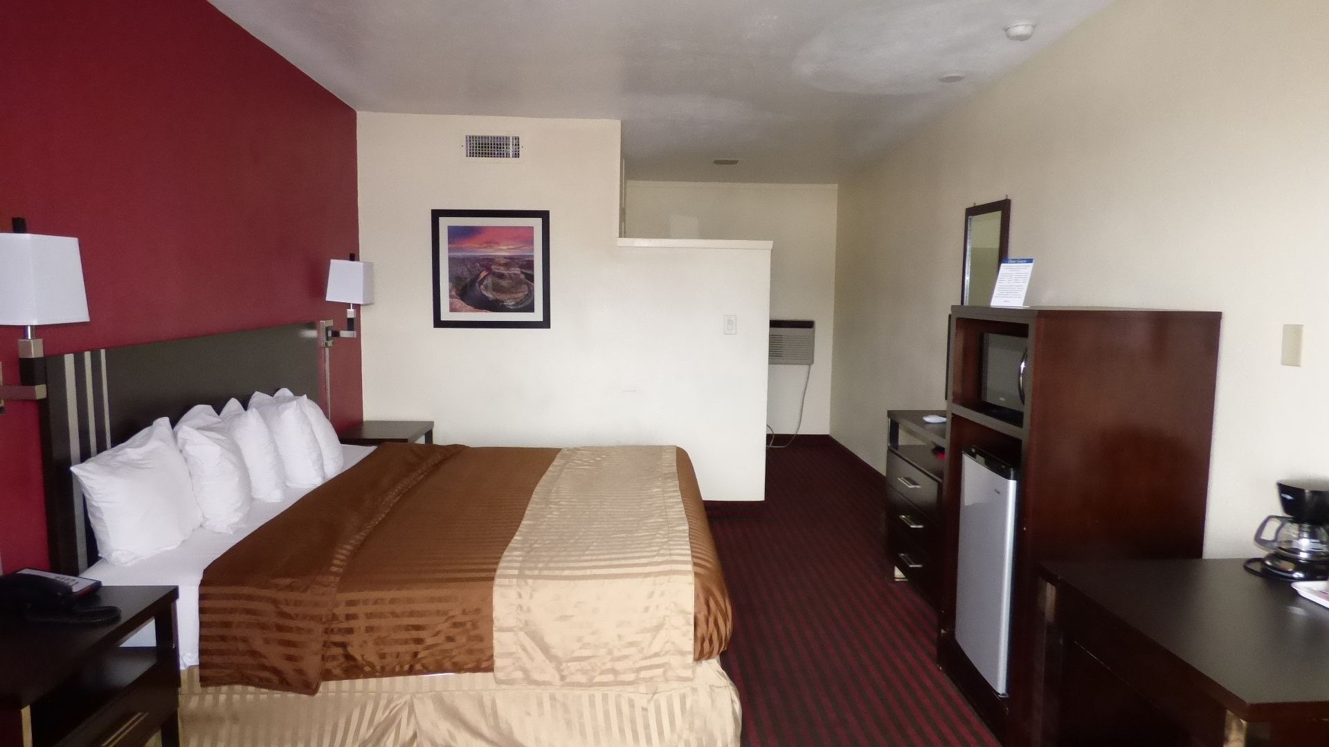 A hotel room with a bed, a desk, a dresser, a refrigerator, and a TV.