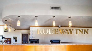 The reception area of the Rodeway Inn with a wooden counter, a clock, and a security camera above the entrance. - Rodeway Inn at Lake Powell (Page)