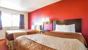 Une chambre d’hôtel avec deux lits, un mur d’accent rouge et une fenêtre avec des rideaux.
