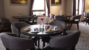 A dining area with round tables and chairs, a vase with flowers, and a menu on the table. - The Priory Hotel (Beauly)