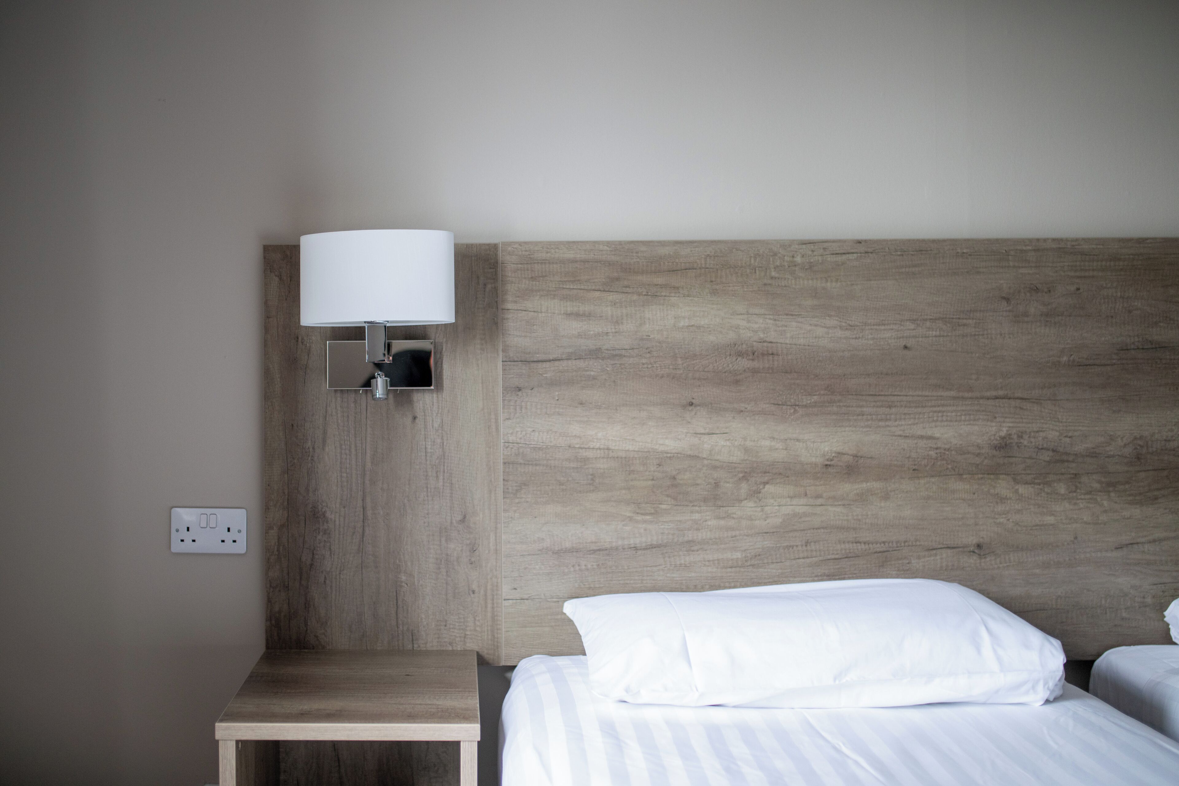 Una habitación de hotel con cabecera de madera, mesita de noche y lámpara.