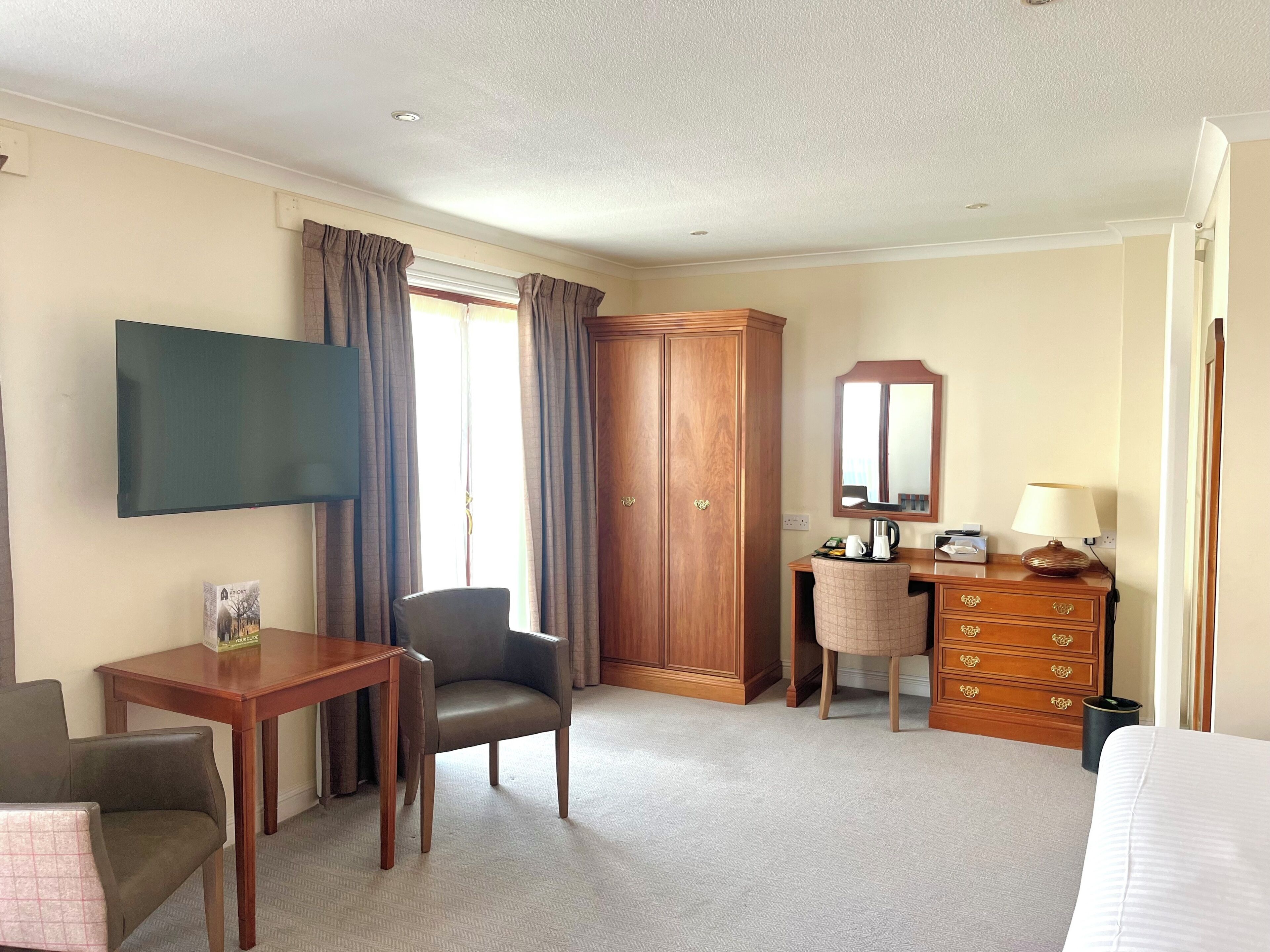 Habitación de hotel con televisor de pantalla plana, armario de madera, escritorio con silla, cómoda con cajones y una cama.