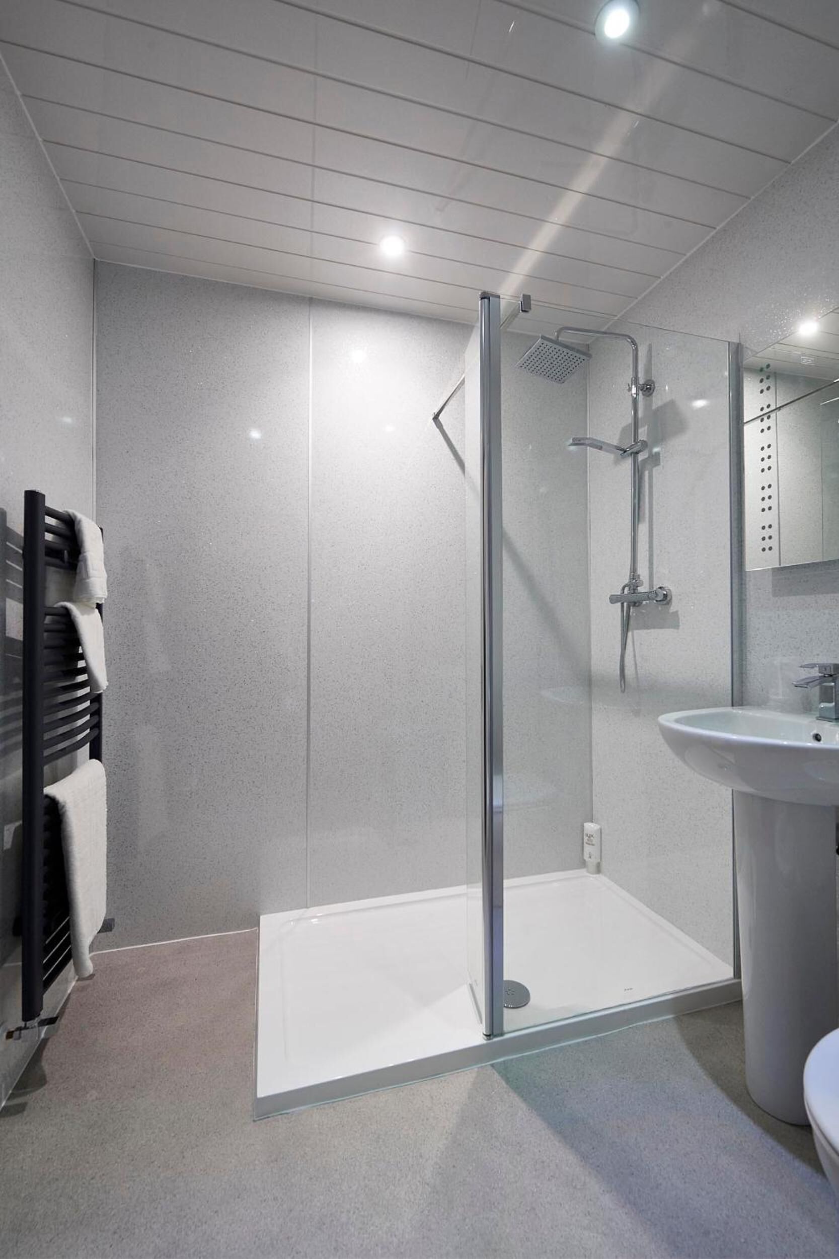 Un baño moderno con ducha envuelta en vidrio, lavamanos blanco y un perchero para toallas.