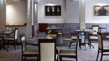 Comedor de hotel con varias mesas y cabinas, amueblado con sillas y mesas, y decorado con centros de mesa florales.
