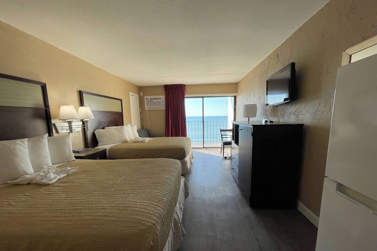 A hotel room with two beds, a desk, a chair, a television, and a view of the ocean.