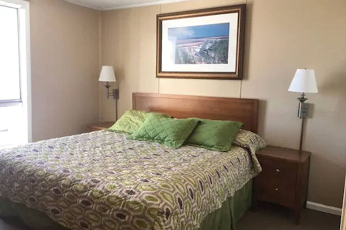 A hotel room with a bed, two bedside lamps, a framed picture on the wall, and a window.