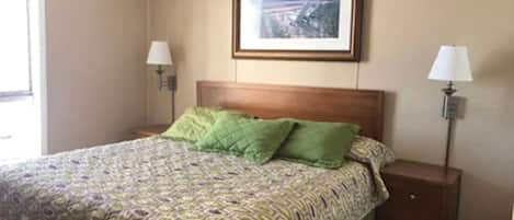 A hotel room with a bed, two bedside lamps, a framed picture on the wall, and a window.