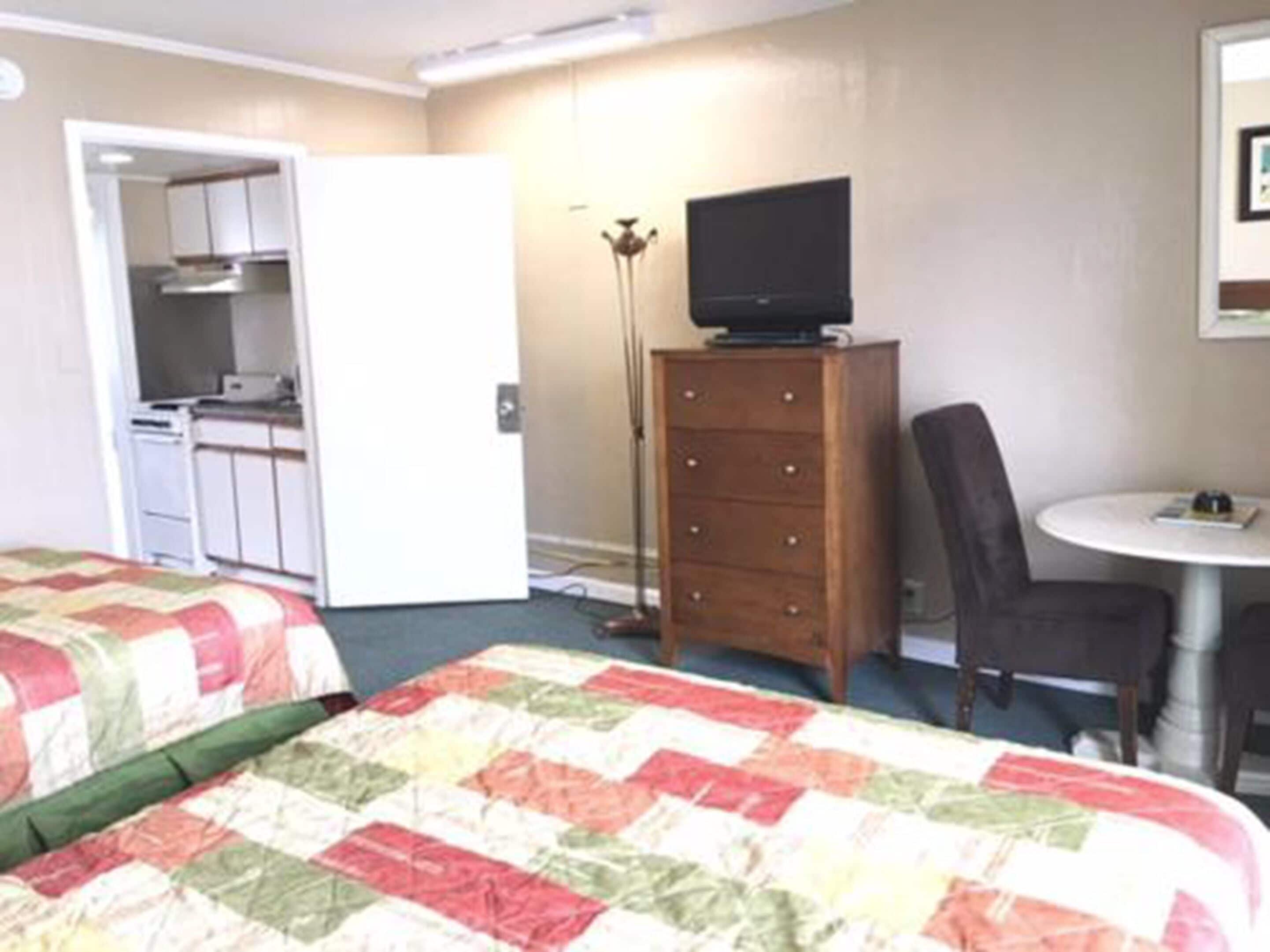 Hotellihuone, jossa on kaksi sänkyä, pieni keittokomero, puinen lipasto, televisio ja pyöreä pöytä, jonka ympärillä on yksi tuoli.