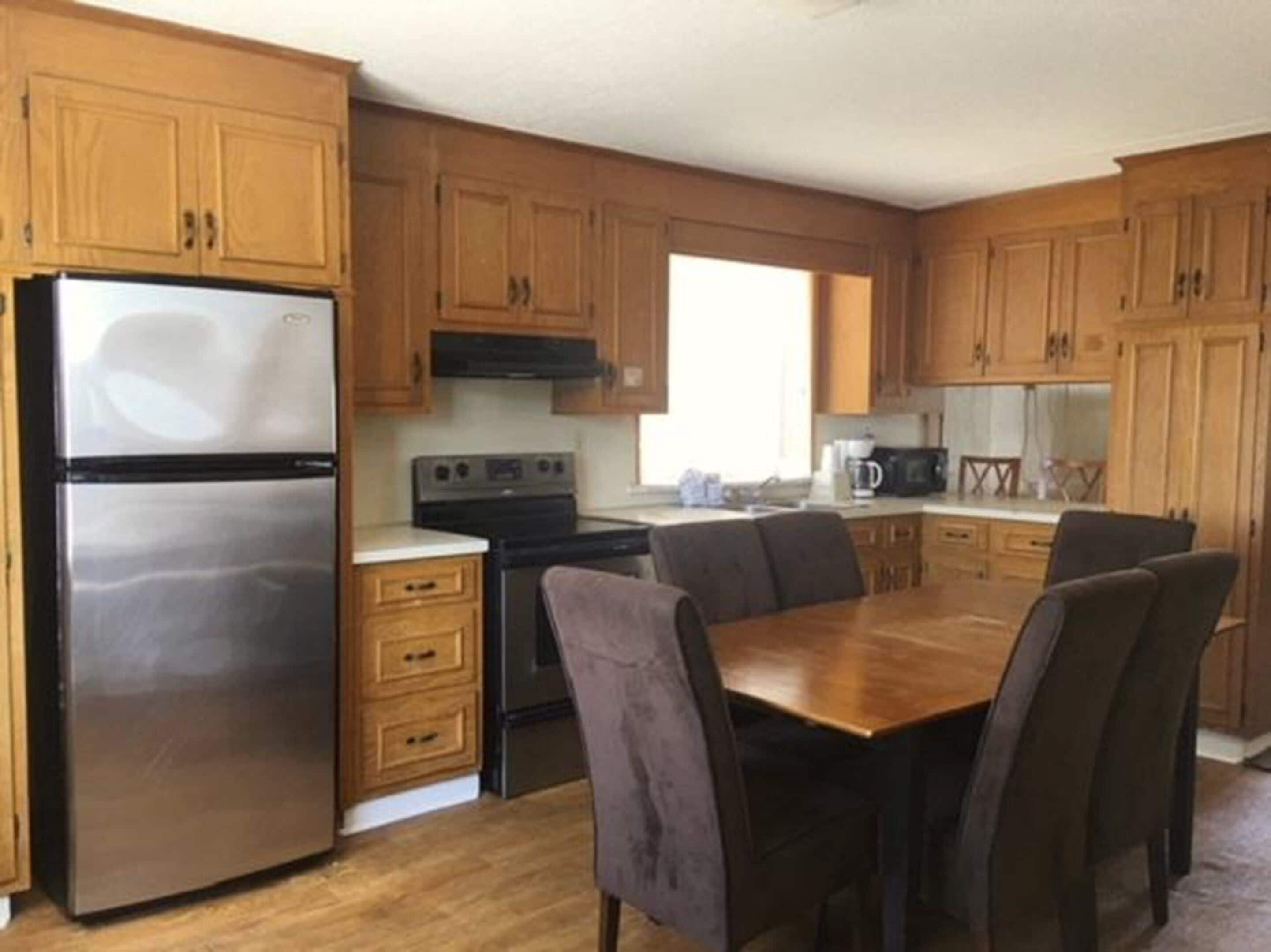 A compact kitchen with wooden cabinets, a stainless steel refrigerator, a stove, and a dining table with chairs.