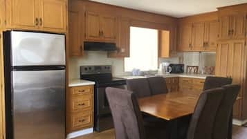 A compact kitchen with wooden cabinets, a stainless steel refrigerator, a stove, and a dining table with chairs.
