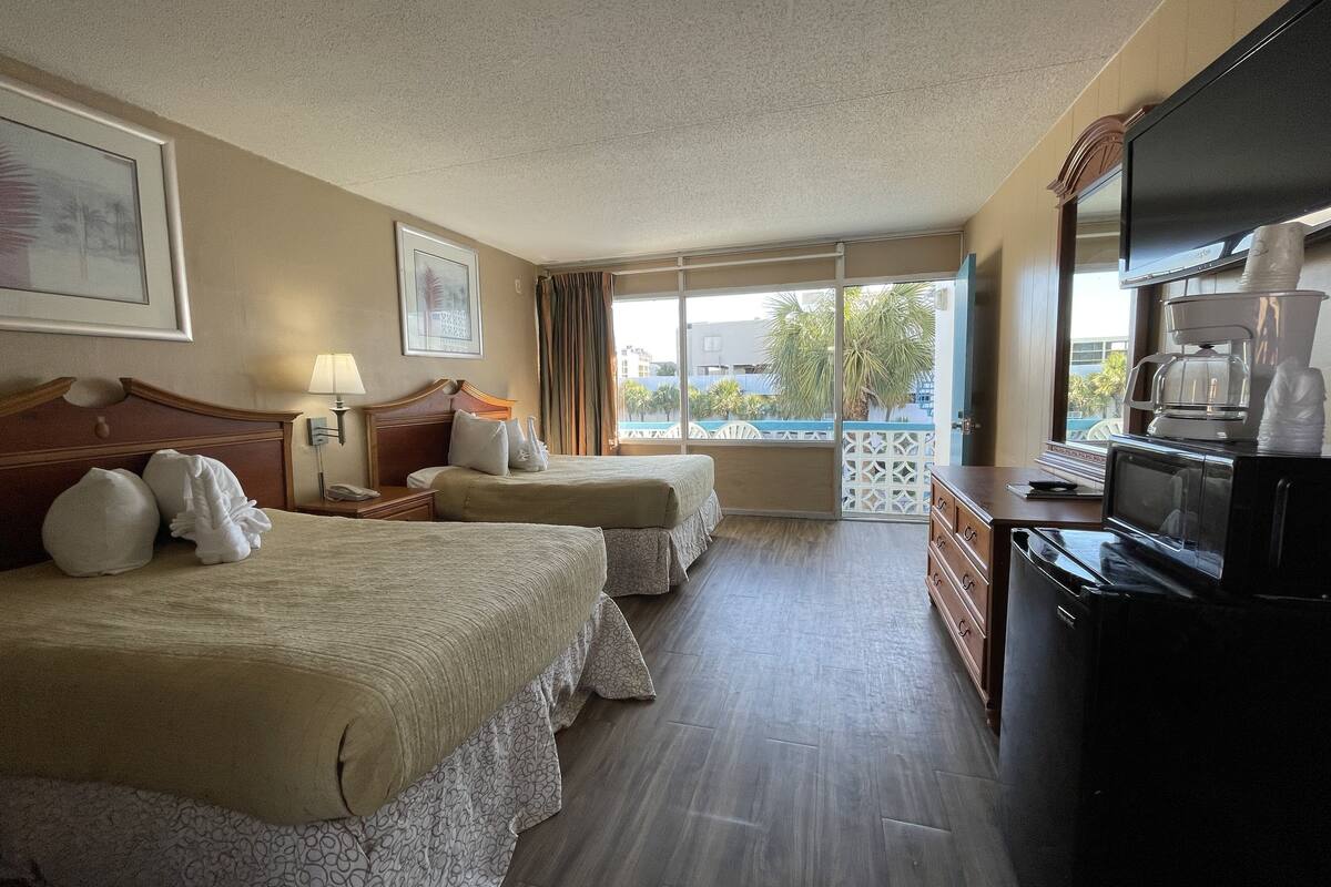 A hotel room with two beds, a TV, a coffee maker, and a view of the outdoors.