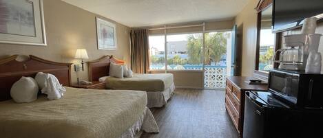 A hotel room with two beds, a TV, a coffee maker, and a view of the outdoors.