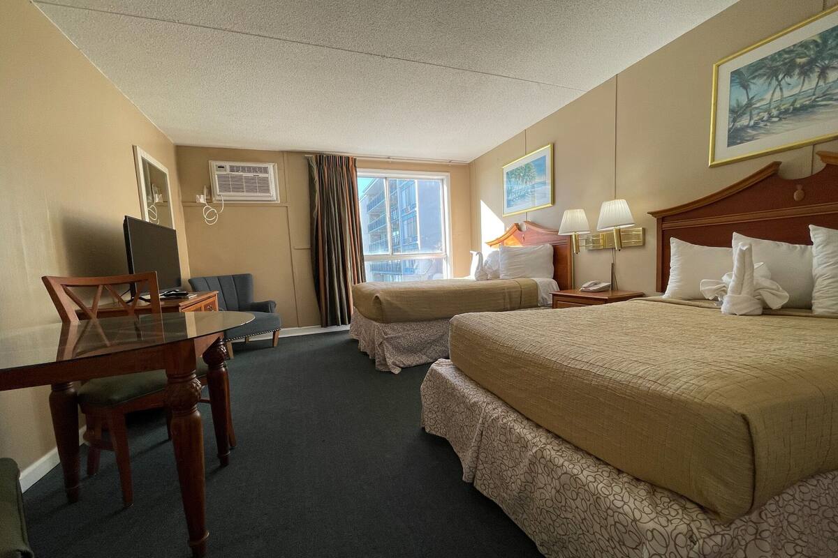 A hotel room with two beds, a desk, a chair, a TV, and a window with curtains.