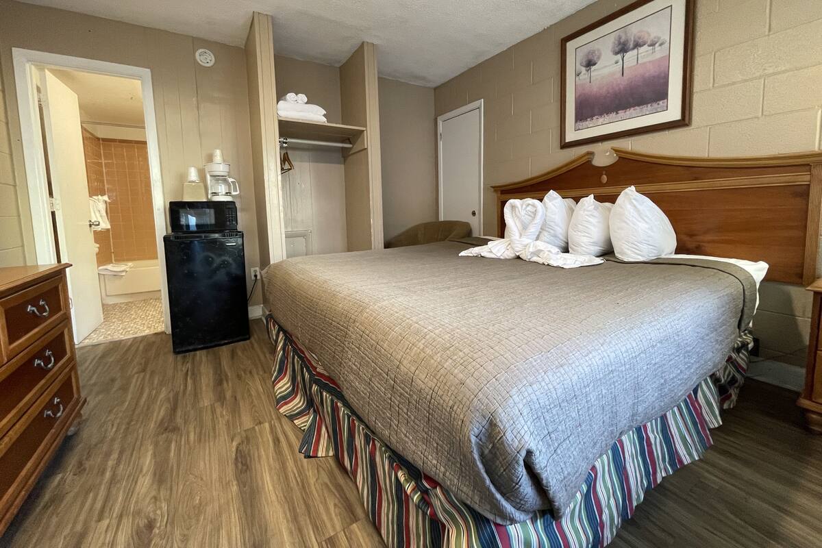 A hotel room with a large bed, a wooden headboard, a coffee maker, a microwave, and a view of the bathroom.