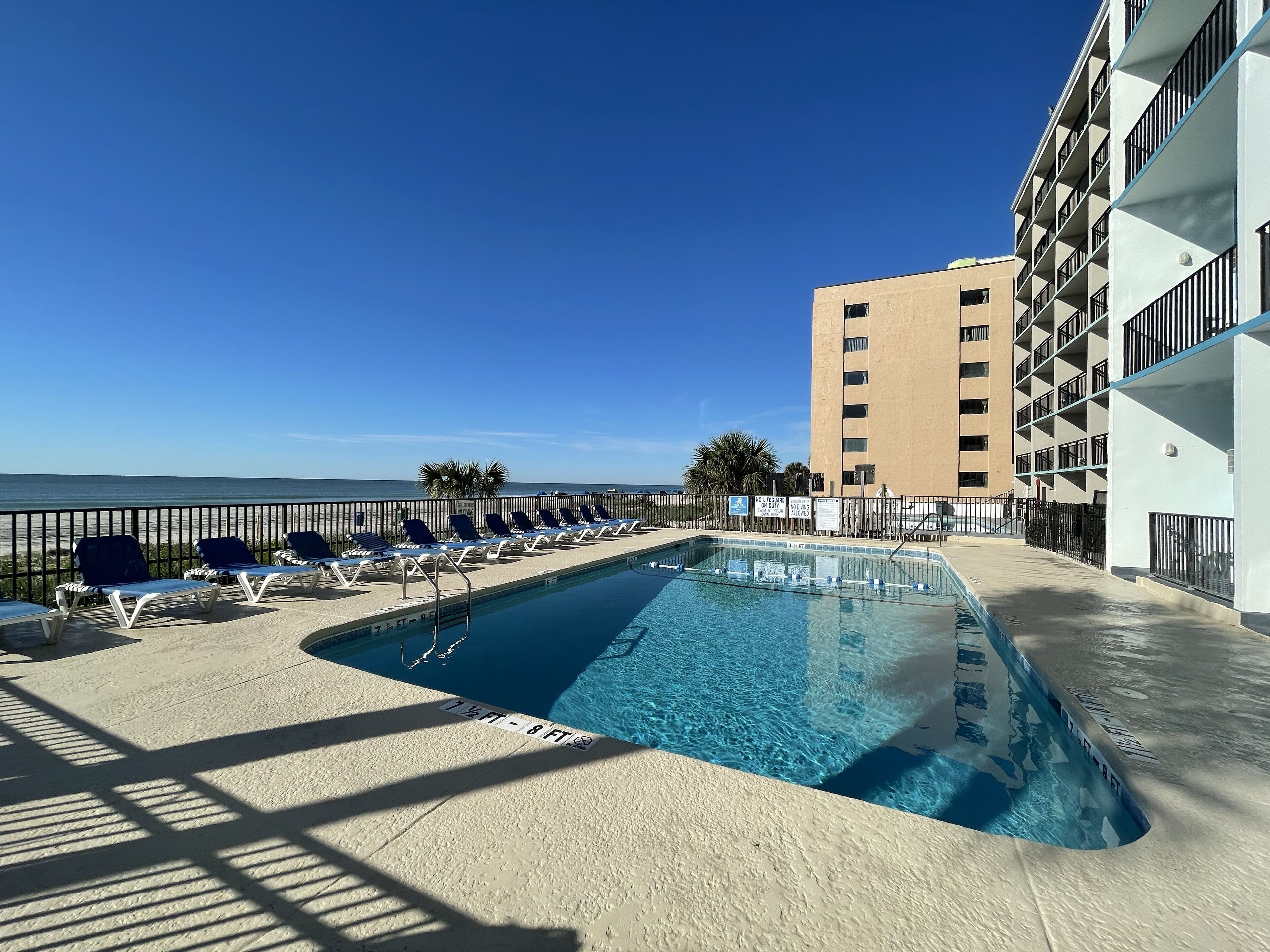 A pool area with lounge chairs and a view of the ocean.