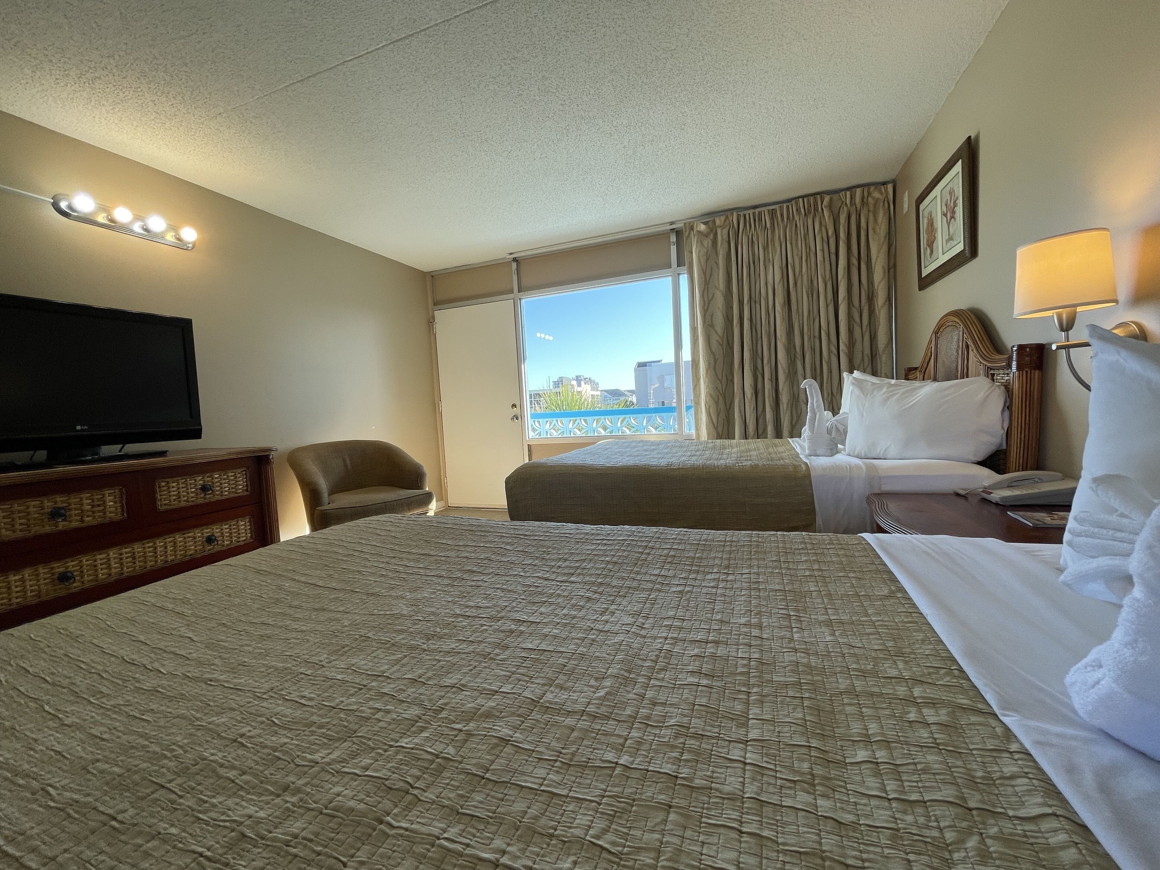 A hotel room with a large bed, a television, a chair, a window with curtains, and a view of the city.