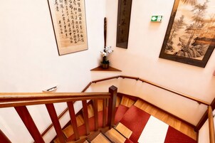 Una escalera de madera con barandilla, un suelo con alfombra de diseño rojo y blanco, y obras de arte en las paredes.