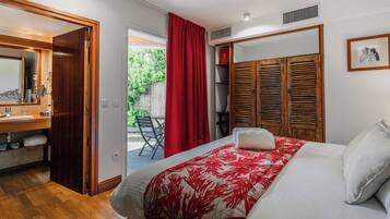 A bedroom with a bed, a wooden wardrobe, a red curtain, and a bathroom with a mirror and sink.