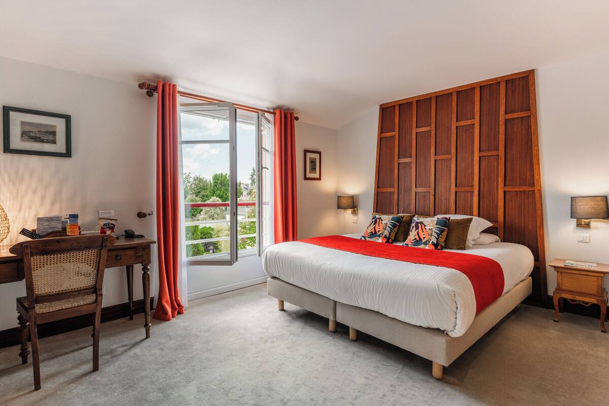 A bedroom with a large bed, a desk, and a window with curtains.