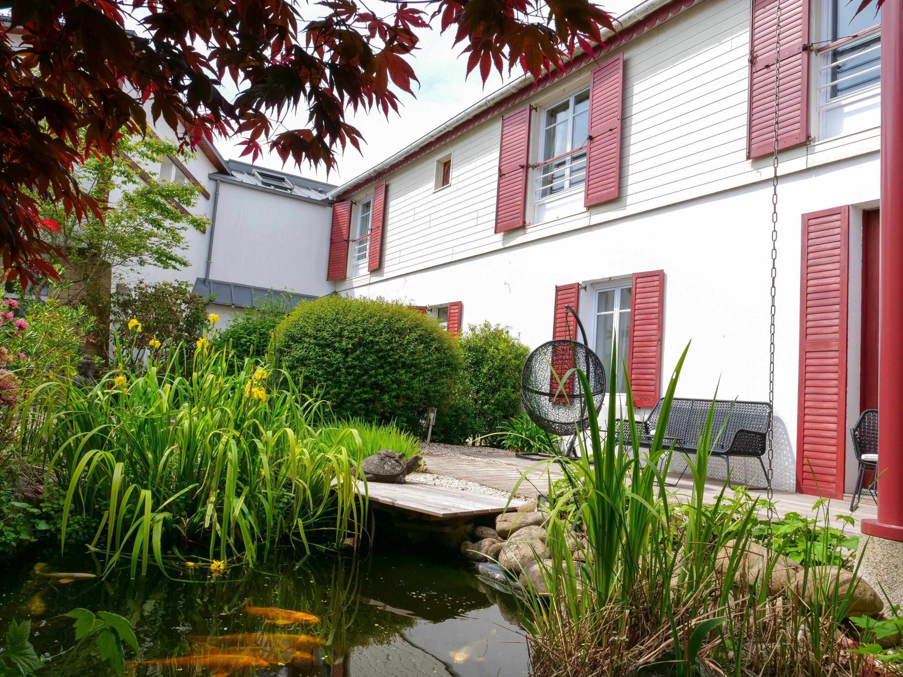 A house with a pond, surrounded by greenery and a wooden deck.