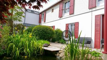 A house with a pond, surrounded by greenery and a wooden deck.