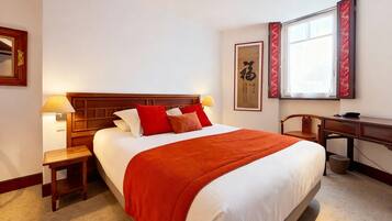 Una habitación de hotel con una cama grande, un escritorio, una silla y una ventana con cortinas rojas.