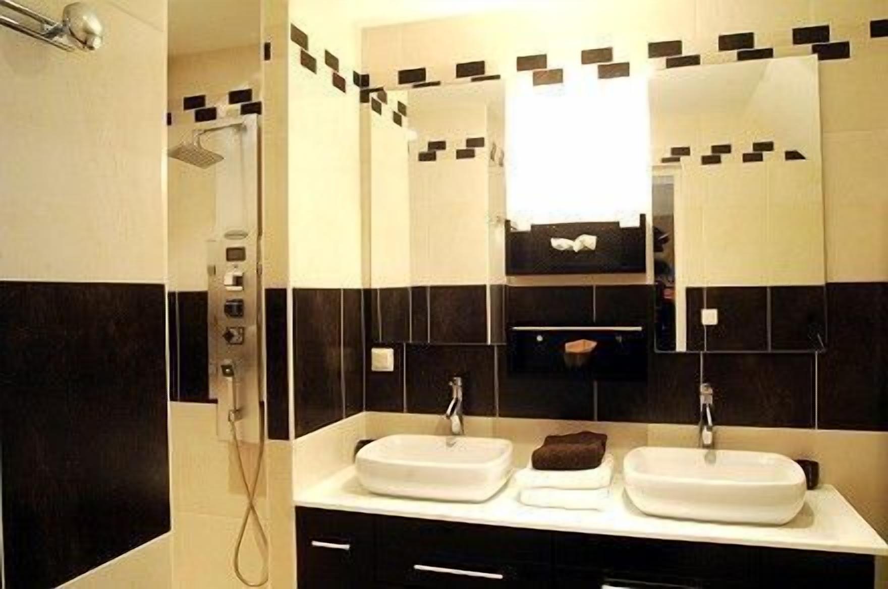 Casa de banho moderna com duas pias, chuveiro e espelho com painel de azulejos a preto e branco.