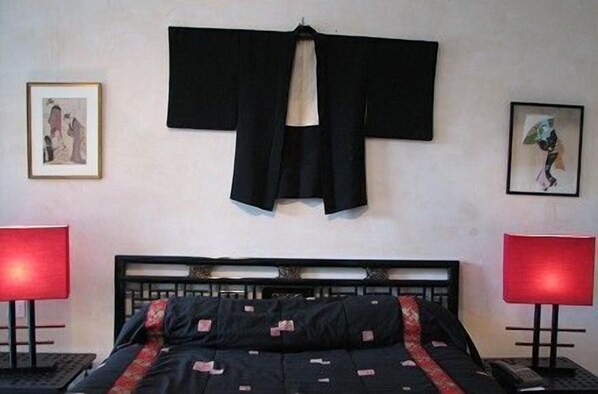 A bedroom with a bed, two bedside tables, a hanging robe, and two framed pictures on the wall.
