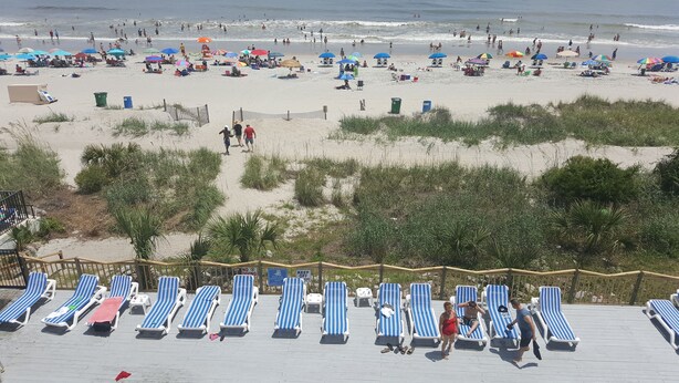 Une plage avec des transats, des parasols et une terrasse en bois dotée de chaises longues.