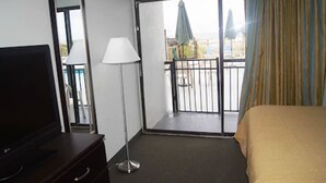Une chambre d’hôtel avec un lit, un téléviseur posé sur une commode, une lampe et un balcon donnant sur l’extérieur.
