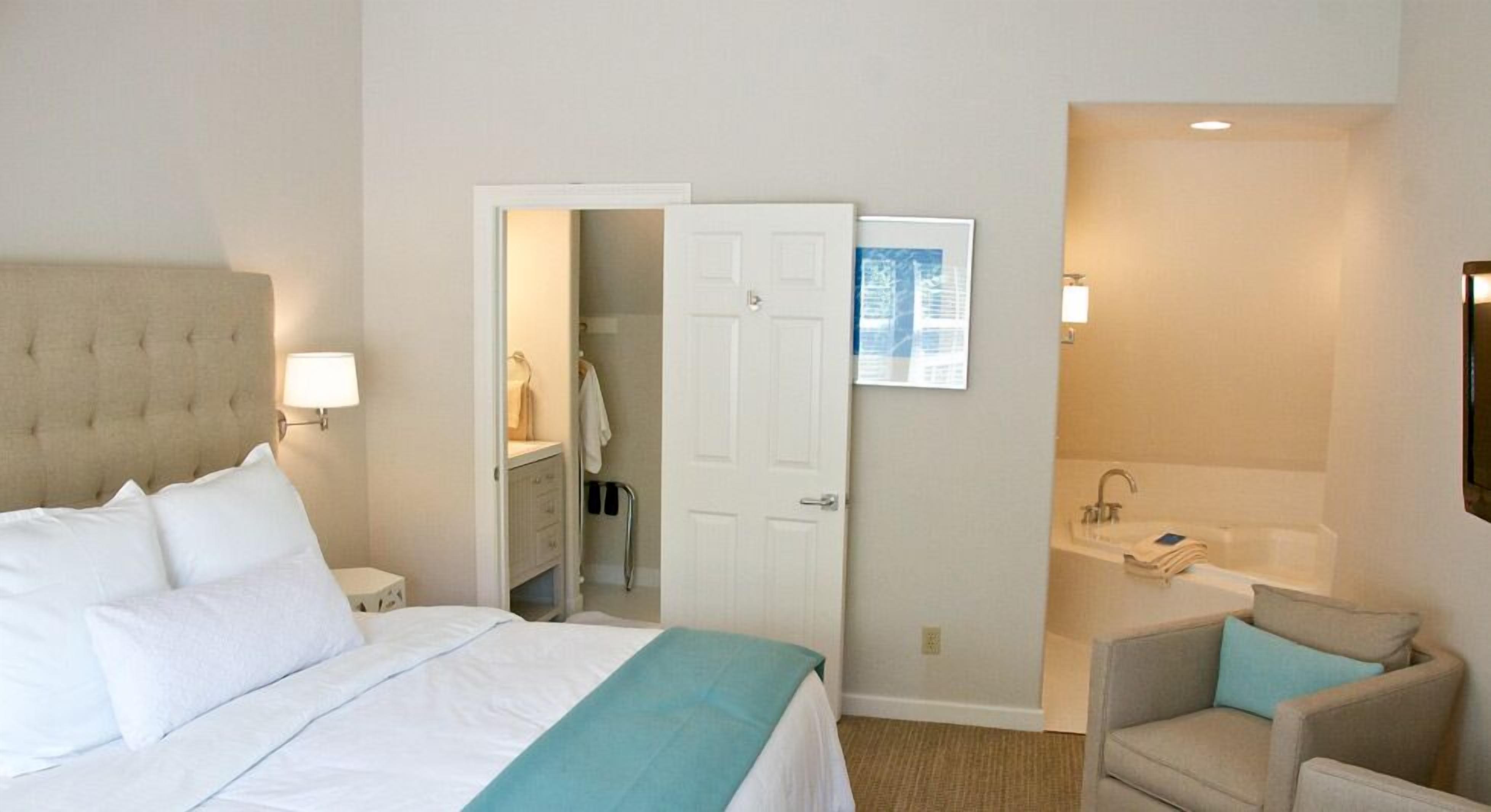 Une chambre d’hôtel comprenant un lit, une chaise, une salle de bain avec un lavabo et une baignoire, et une porte donnant sur un placard.
