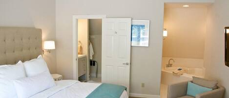 A hotel room with a bed, a chair, a bathroom with a sink and bathtub, and a door leading to a closet.