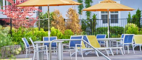 A poolside area with lounge chairs and umbrellas, a pool, and a garden with pink flowering trees.