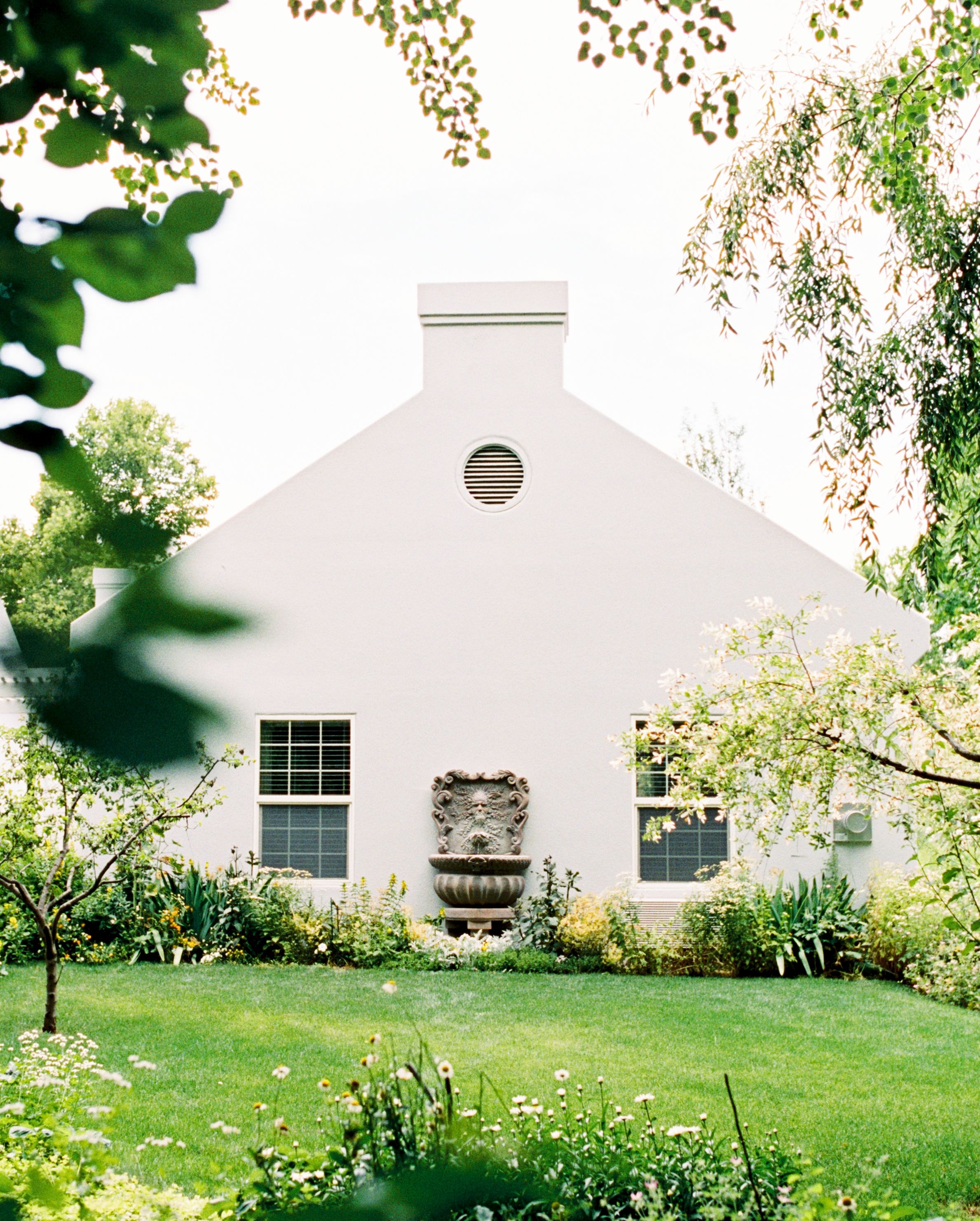 A white building with a triangular roof, a circular window, and a stone fountain in the center.