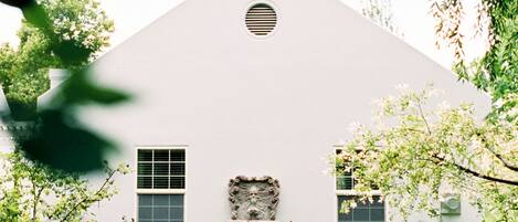 A white building with a triangular roof, a circular window, and a stone fountain in the center.