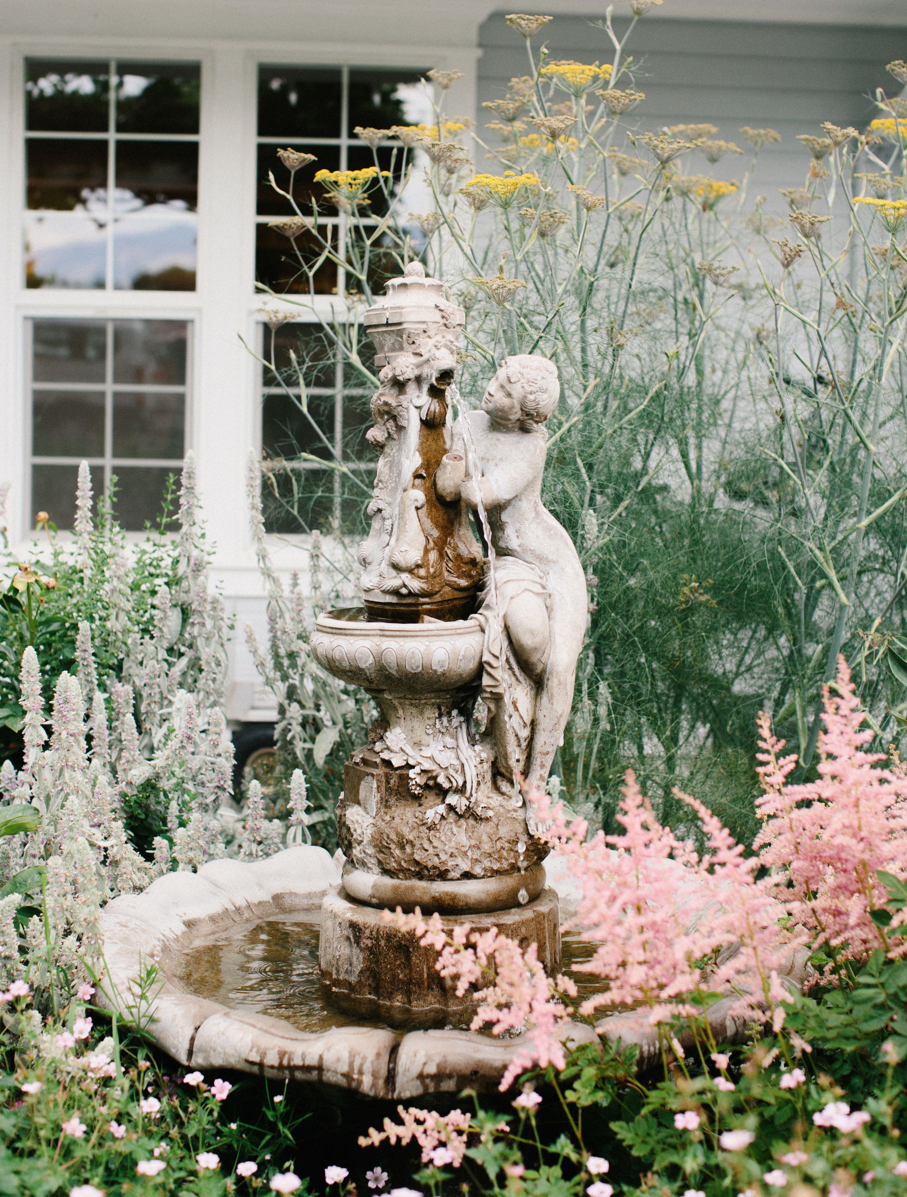 Un giardino con una fontana, circondato da diverse piante e fiori.