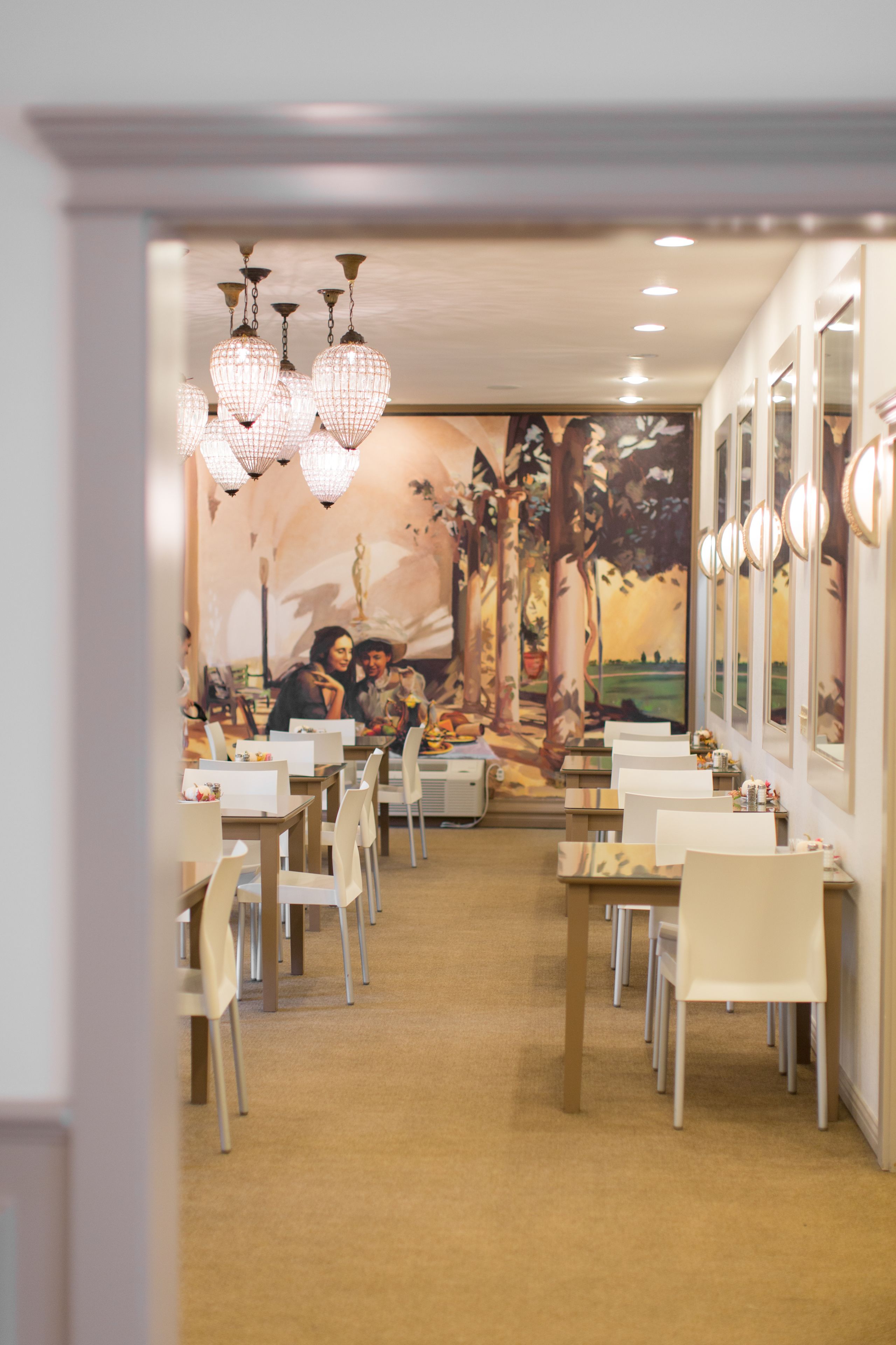 Ein Restaurant mit Wandgemälde einer sitzenden Paar, Kronleuchtern und weißen Stühlen.