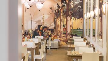A restaurant with a mural of a couple on a bench, chandeliers, and white chairs.