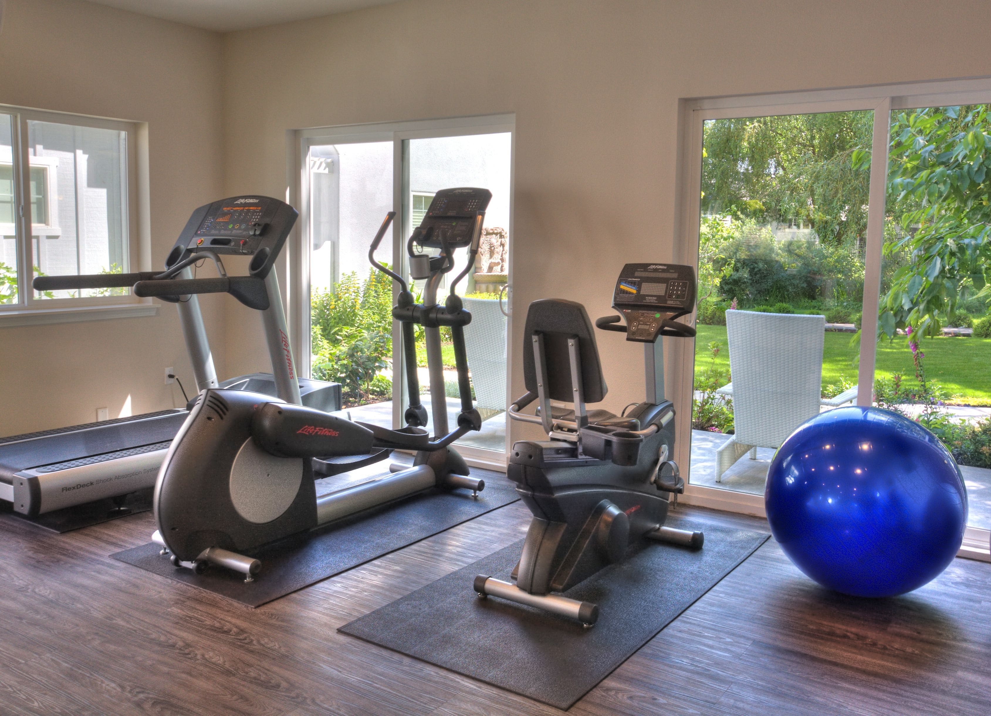 Uma academia em casa com esteira, elíptico, bicicleta ergométrica e uma bola de exercícios azul.
