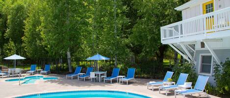 A swimming pool with lounge chairs and umbrellas, surrounded by trees and a building with a balcony.
