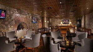 Un salon spacieux avec un mur en pierre rustique, des sièges confortables, un coin bar et un écran de télévision.