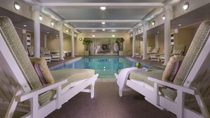 Un espace piscine agrémenté de deux chaises longues disposées face à la piscine, entouré de colonnes blanches et doté d’un plafond avec des luminaires encastrés.
