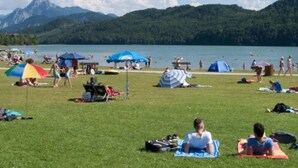 A grassy area with people relaxing under umbrellas, a lake, and mountains in the background. - Appartementhotel Seespitz (Fuessen)